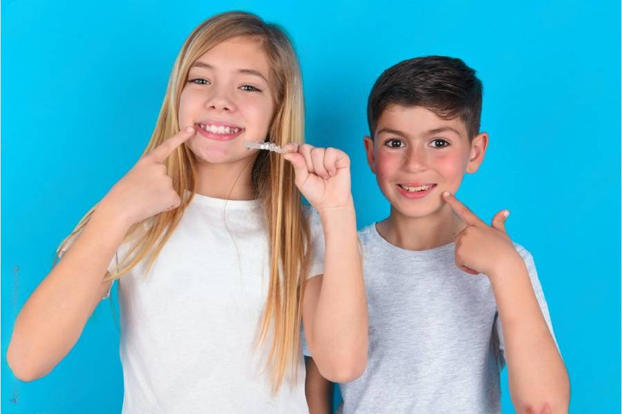 Dečak i devojčica se smeju i pokazuju zube, držeći Invisalign folije u rukama.