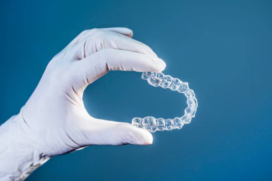 Širok kadar ruke u beloj rukavici koja drži Invisalign folije.