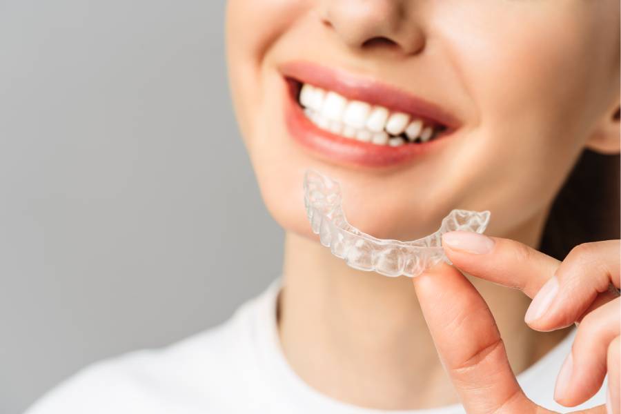 Krupan kadar ispravljenog osmeha devojke koja drži Invisalign foliju u rukama.